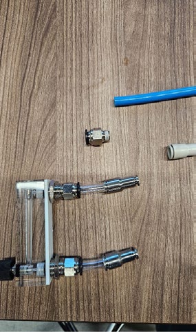An acrylic panel flowmeter with two push-to-connect fittings, short 10 mm tubes and reducers to 6 mm tubing